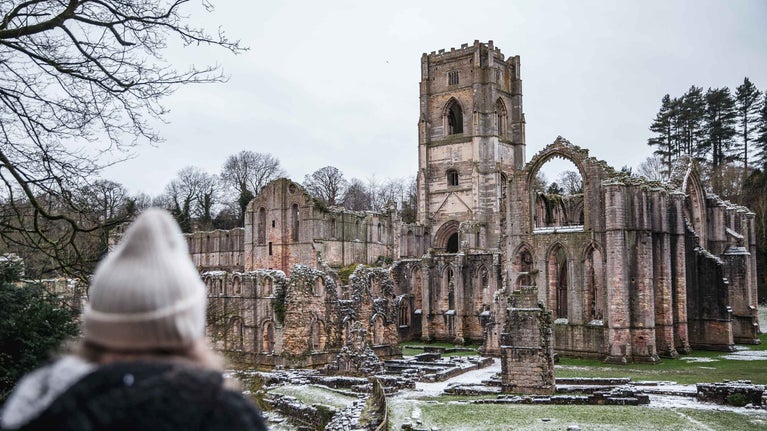 Person looking at Fountains Abbey from de greys walk on a snowy day